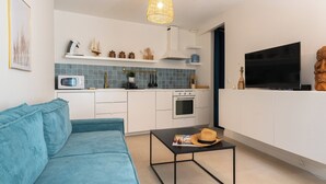 Una cocina moderna con armarios blancos, un microondas y una estufa. Hay un sofá azul y una mesita con un sombrero encima.