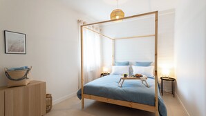 Una cama con dosel con un edredón azul, una mesita de noche con una lámpara y una cesta de mimbre sobre un aparador de madera.