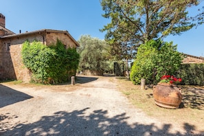 A rustic stone building with a gravel driveway leading to a wooden gate. - Villa Capanna: A Window onto Tuscany (Vico dʼArbia)
