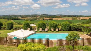 Une piscine entourée d’une clôture en bois, avec des chaises longues et une vue sur la campagne.