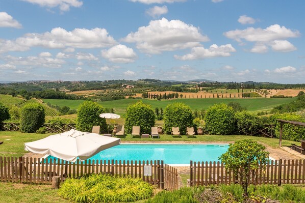 Ein Schwimmbecken mit Holzumzäunung, Liegestühlen und Blick auf die Landschaft.