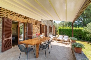 Eine Terrasse im Freien mit einem Holztisch und -stühlen, einer Rattan-Couch und einem Blumentopf.