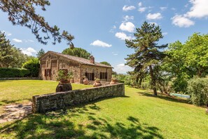 A stone building with a tiled roof, surrounded by a well-maintained lawn and trees.