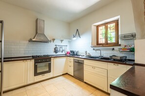Une cuisine avec des meubles blancs, une cuisinière, un four et un lave-vaisselle. Il y a une fenêtre donnant sur un paysage verdoyant.