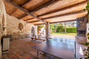 Une table de ping-pong, des murs en pierre, des poutres en bois, une cheminée en pierre et un banc.
