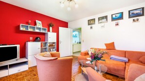 Een woonkamer met een rode wand, een wit kastje, een televisie en een oranje bank.
