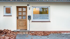 Een huis met een houten deur, een raam met een witte omlijsting, en een brievenbus op de muur.