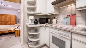 Een compacte keuken met een magnetron, koffiezetapparaat en een klein oven. In de aangrenzende kamer staat een bed met een houten hoofdbord.