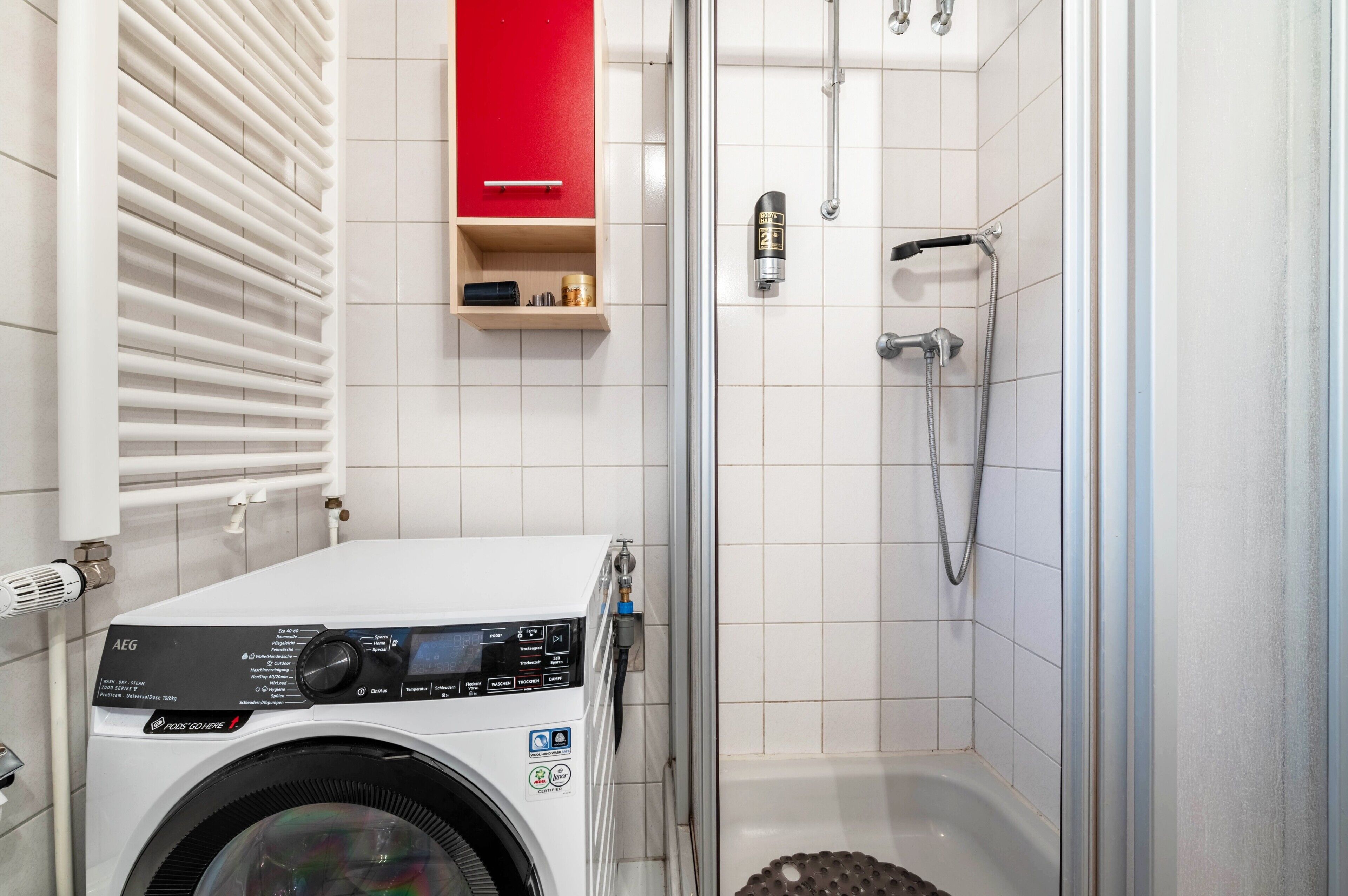 A compact bathroom with a washing machine, a shower, and a red cabinet.