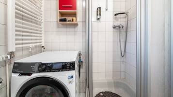 A compact bathroom with a washing machine, a shower, and a red cabinet.