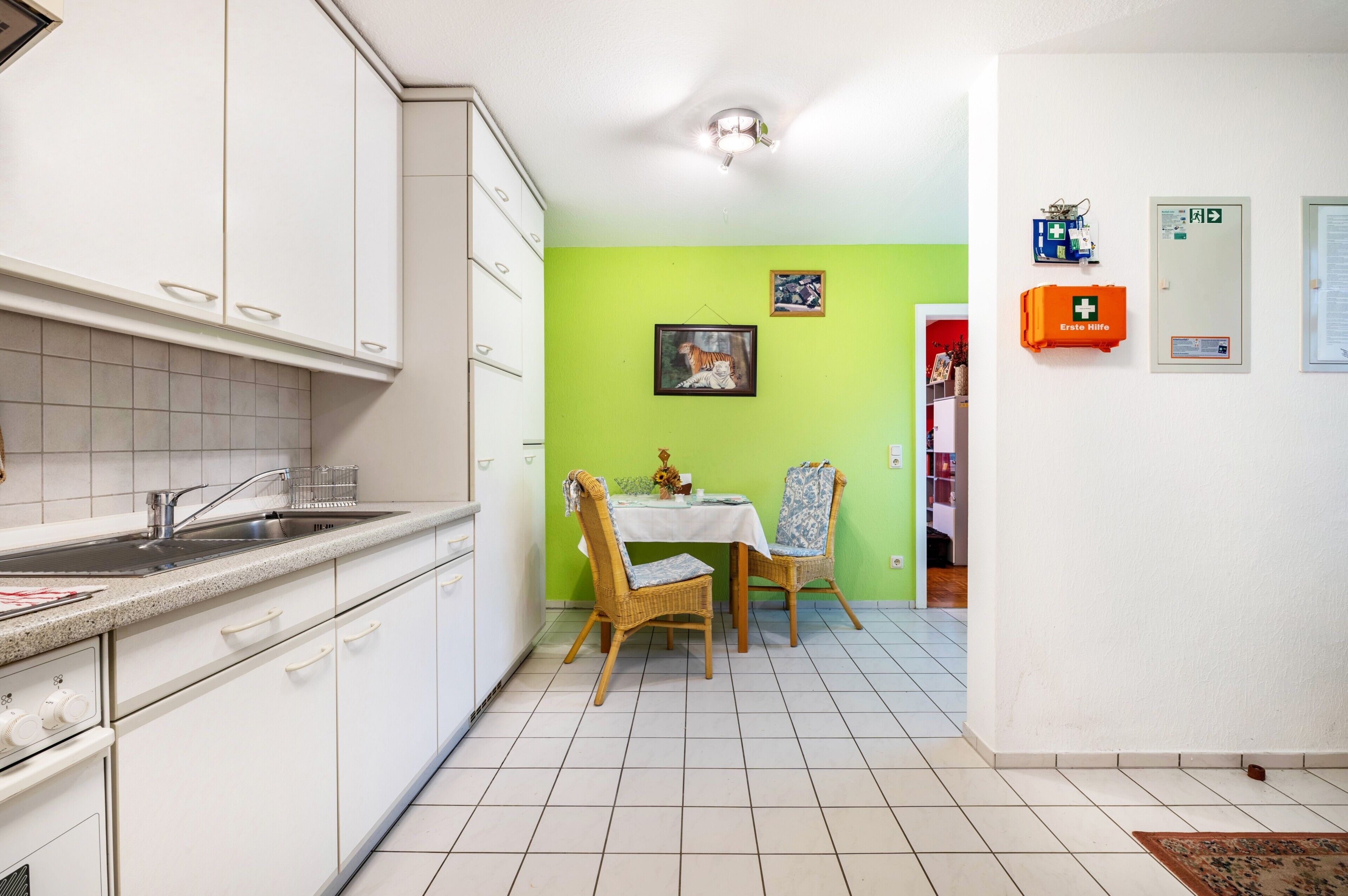 Eine Küche mit weißen Schränken, einem Esstisch mit zwei Stühlen, einer grünen Wand und einem kleinen Tisch mit einer Vase.