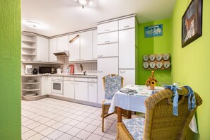 Une cuisine avec des meubles blancs, un four à micro-ondes et un évier. On y trouve une table à manger avec des chaises et un vase rempli de fleurs.