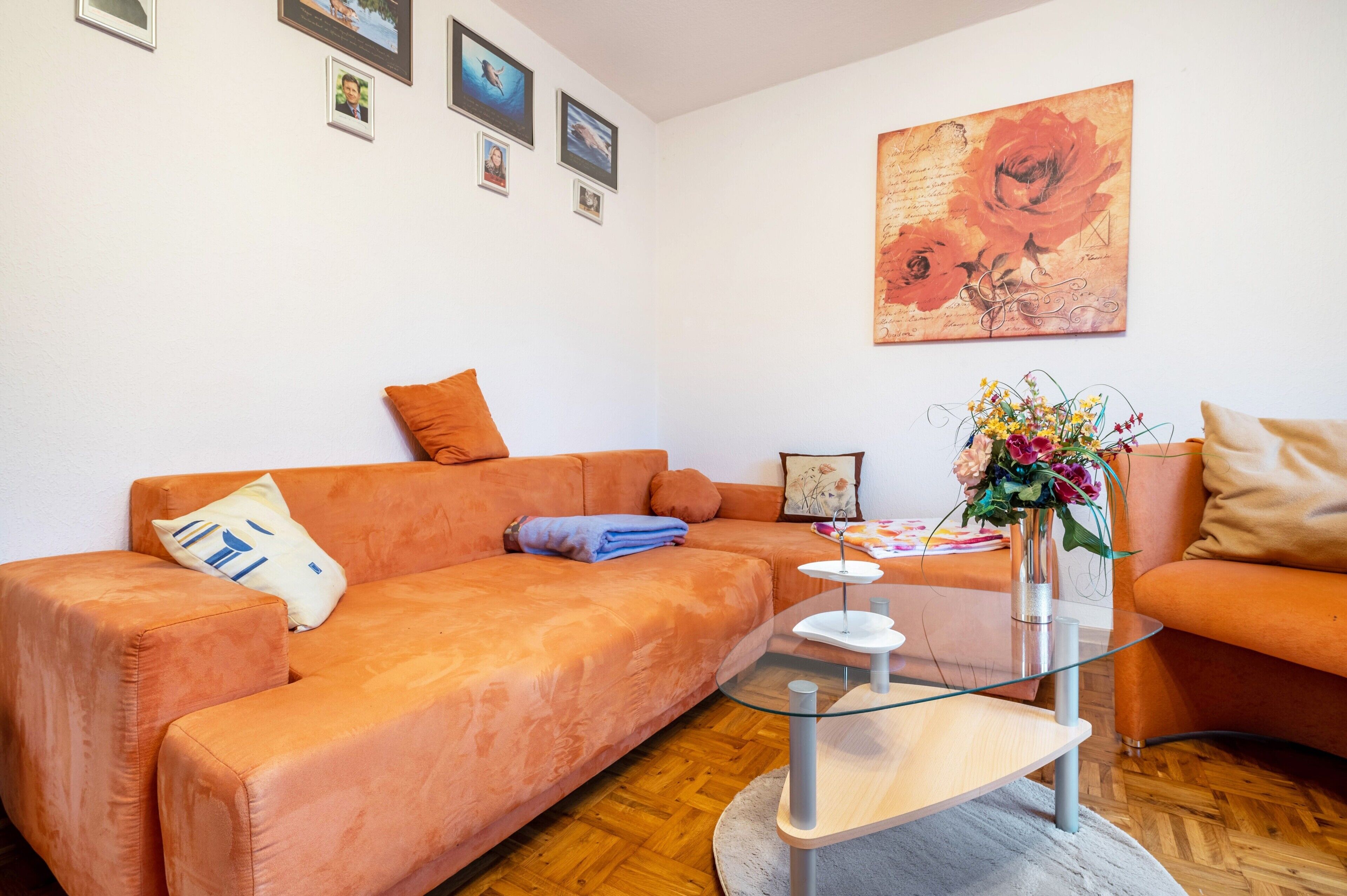 Een woonkamer met een bank, een glazen bijzettafeltje en een schilderij aan de muur.