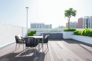 Um terraço no telhado com mesa, cadeiras, churrasqueira e plantas em vasos.