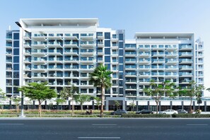 Um hotel moderno de vários andares com varandas, área de estacionamento e palmeiras.