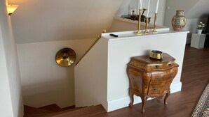 A staircase with a white wall, a wooden cabinet with drawers, a brass lamp, and a vase on a white console table. - Holiday Home 'Feel at Home in Different Spaces' with Wi-Fi (Heide)