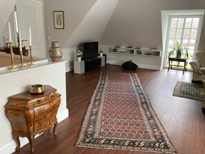 A living room with a wooden floor, a large patterned rug, a television, a bookshelf, and a door leading to a balcony. - Holiday Home 'Feel at Home in Different Spaces' with Wi-Fi (Heide)