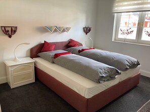 A double bed with grey and red bedding, a bedside table with a lamp, and wall-mounted decor. - Holiday Home 'Feel at Home in Different Spaces' with Wi-Fi (Heide)