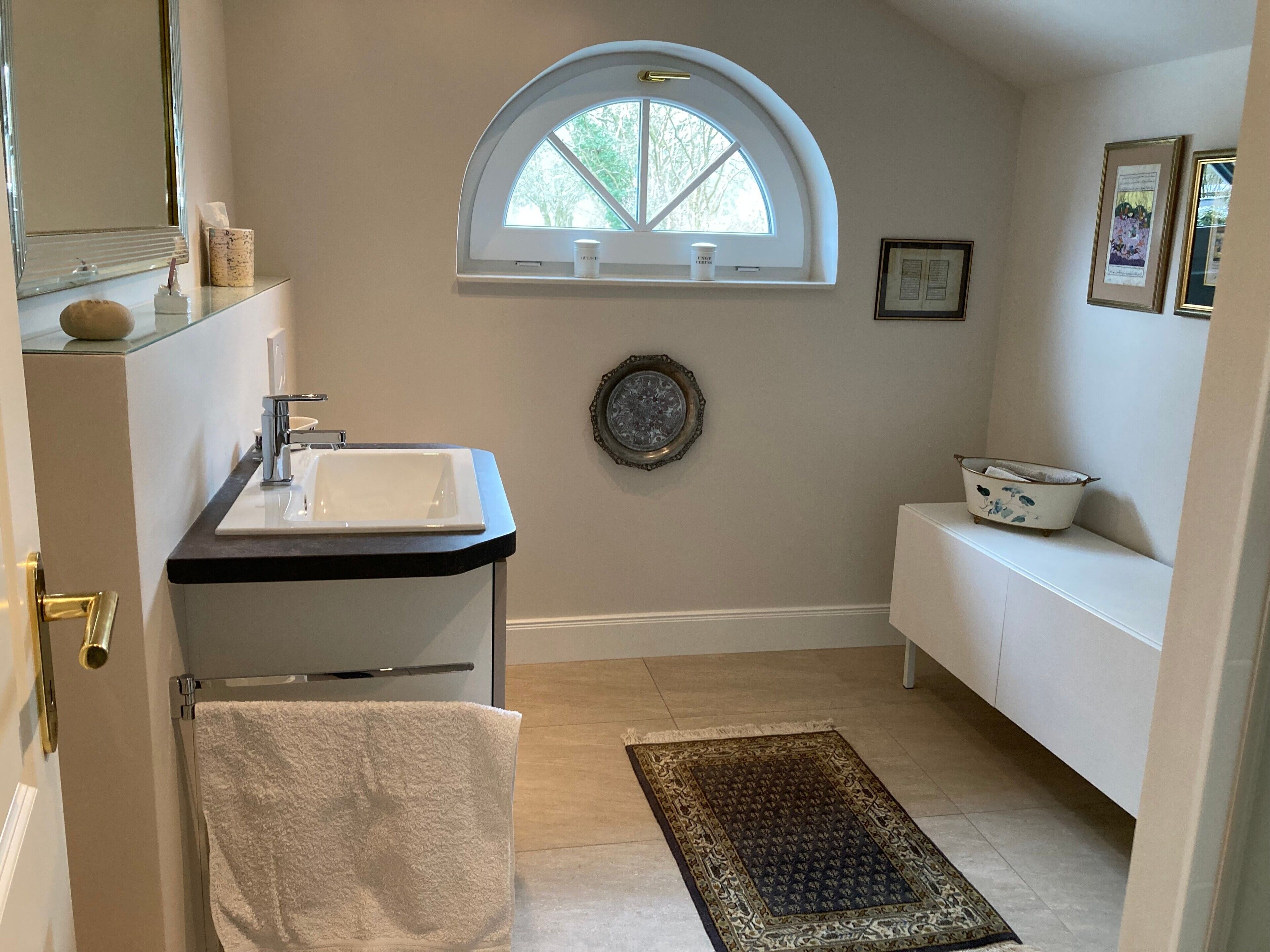 A bathroom with a sink, mirror, window, towel rack, and a decorative plate on the wall.