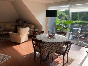 A modern living room with a dining table, chairs, a sofa, a floor lamp, and a large window with a view of greenery. - Holiday Home 'Feel at Home in Different Spaces' with Wi-Fi (Heide)