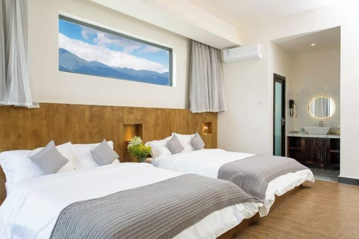 Una habitación de hotel con dos camas, un ventanal con vistas a la montaña, un cabecero de madera y un baño visible a través de una puerta abierta.