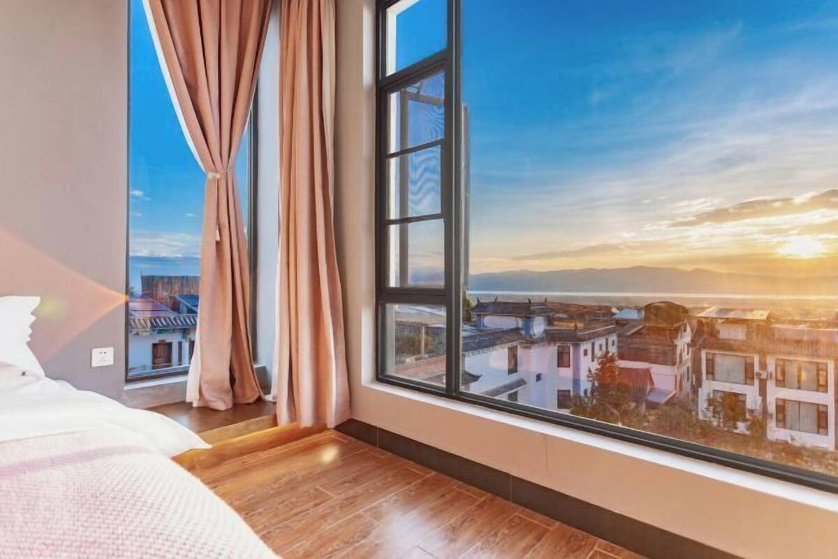 Un dormitorio con un ventanal grande, suelo de madera y vistas a edificios tradicionales.