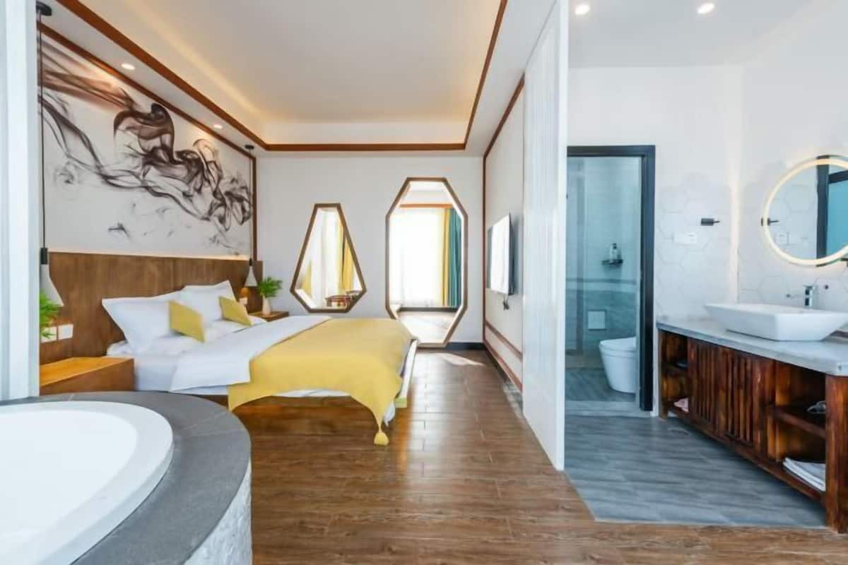 Una habitación de hotel moderna con una cama, un baño con lavabo y espejo, y un ventanal grande.