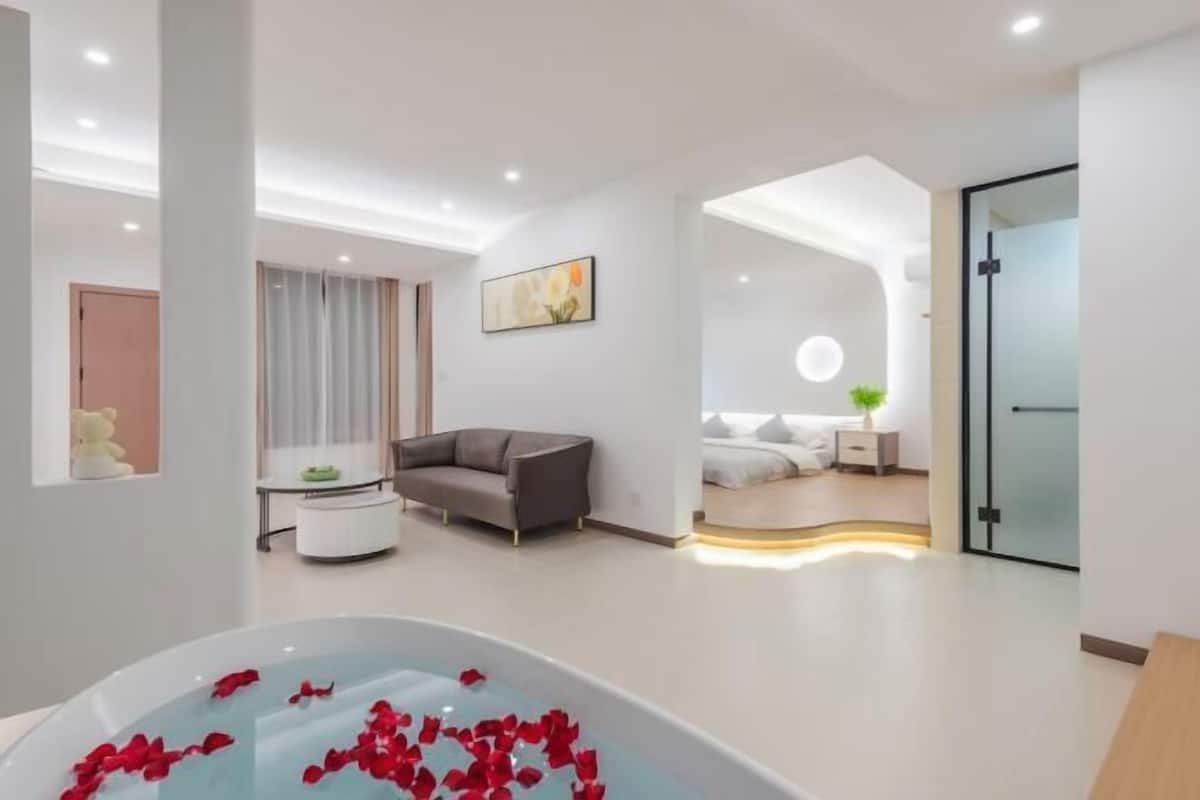 Una habitación de hotel moderna con una bañera grande, un sofá, un comedor y un dormitorio con cama y mesita de noche.