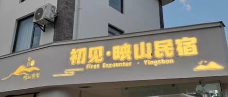 A hotel with a modern facade, a prominent sign with Chinese characters, and an air conditioning unit mounted on the exterior wall.