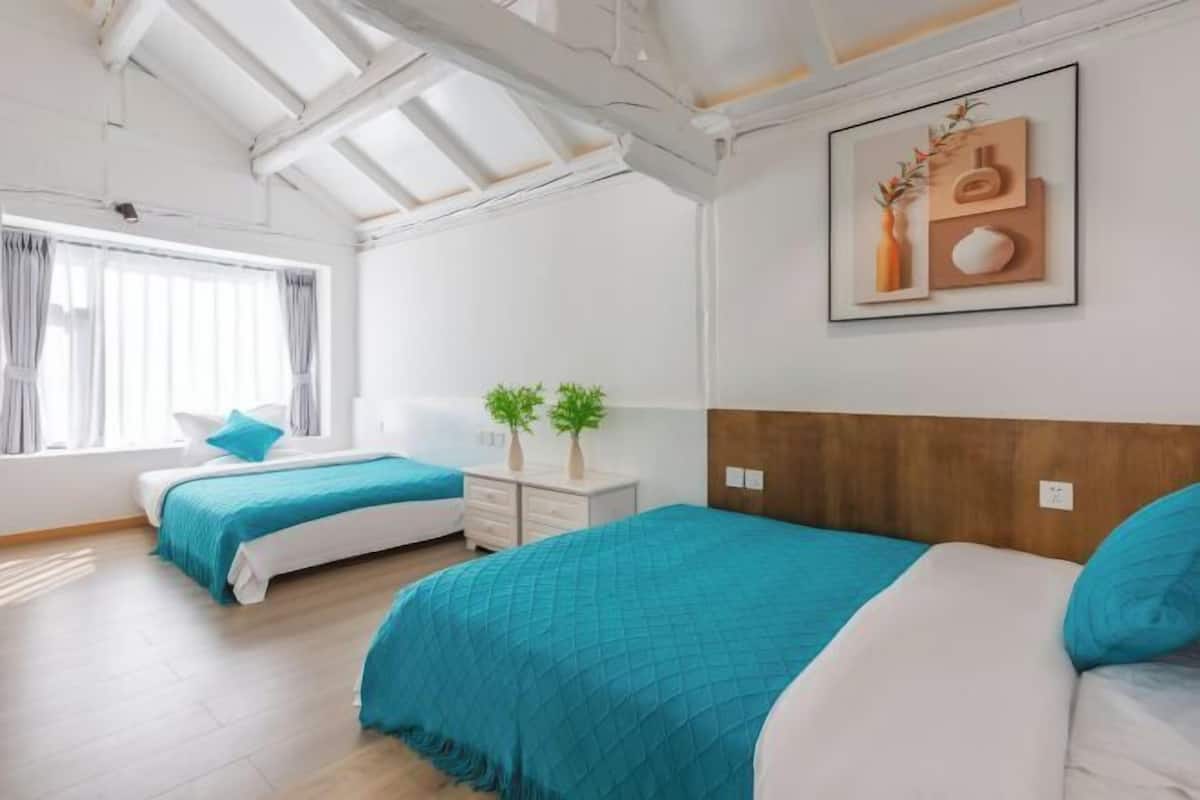 Un dormitorio moderno con dos camas, un tragaluz, un cuadro y una planta pequeña en la mesita de noche.