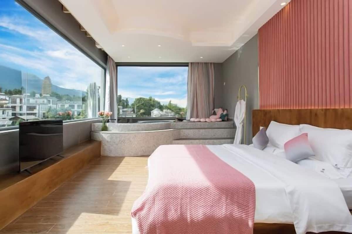 Una habitación de hotel moderna con una cama grande, un televisor y vistas a un paisaje urbano y montañas.