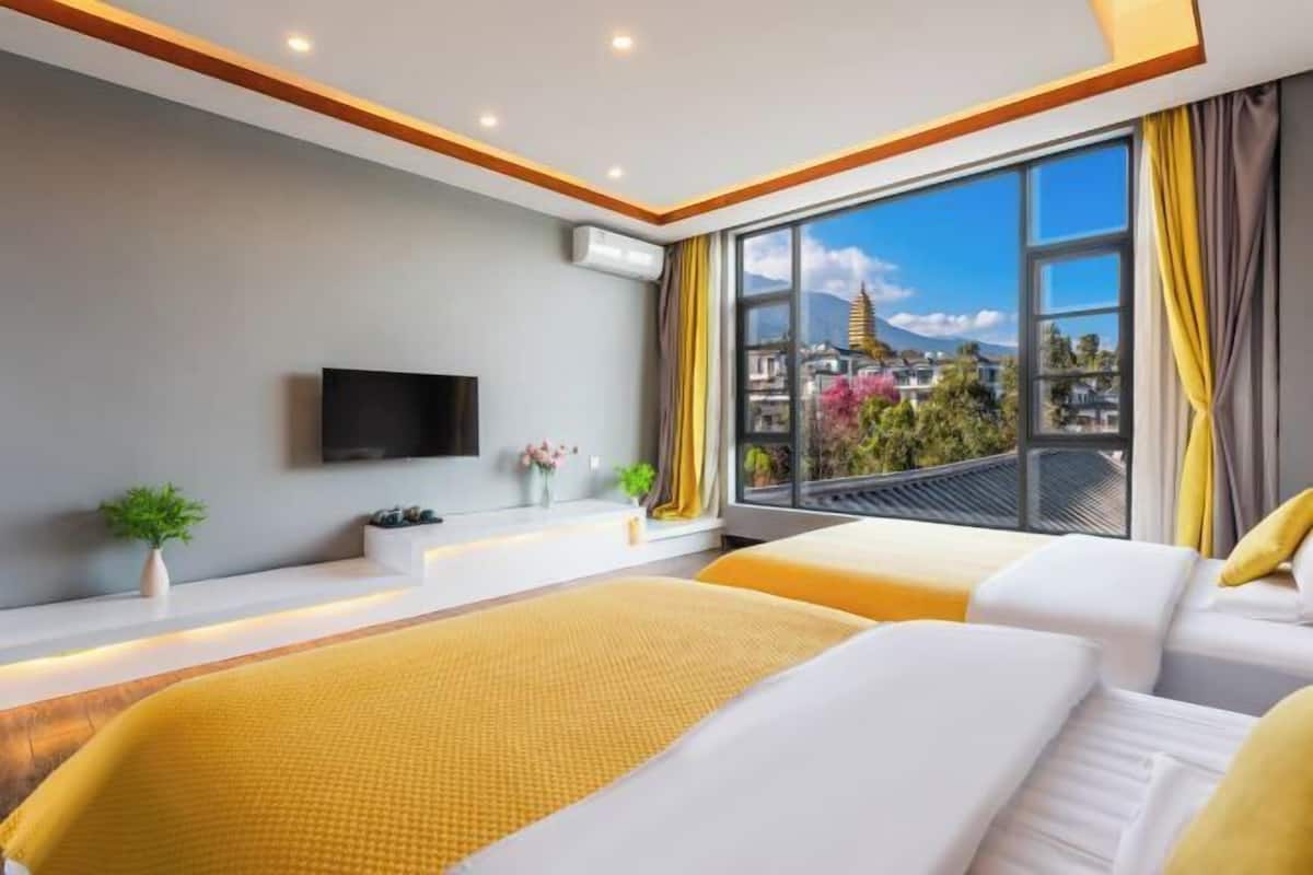 Una habitación de hotel moderna con dos camas, un amplio ventanal con vistas a la ciudad, un televisor de pantalla plana en la pared y una pequeña planta en el alféizar.