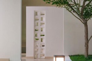 Un interior minimalista con un separador blanco, un pequeño árbol y una banca.