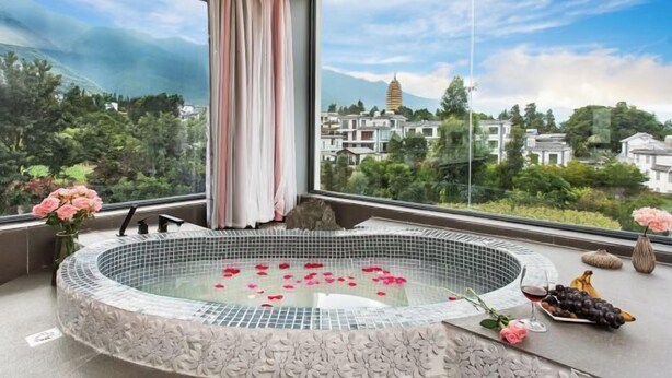 A spa room with a hot tub, a view of a mountain, and a balcony with flowers and fruit. - First Sight Yingshan Resort (Dali)