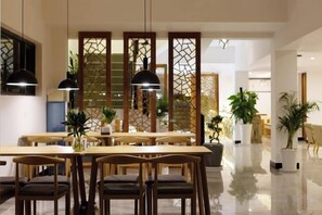 A modern dining area with wooden tables and chairs, pendant lighting, and potted plants. - First Sight Yingshan Resort (Dali)