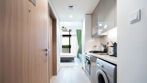 A modern kitchen with a washing machine, a dining area with a table and chairs, and a bedroom with a bed and curtains. - Modern Studio in Azizi Riviera 46  (Dubai)