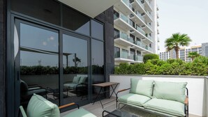 A modern outdoor seating area with a glass table and chairs, a sofa, and a small table. - Modern Studio in Azizi Riviera 46  (Dubai)
