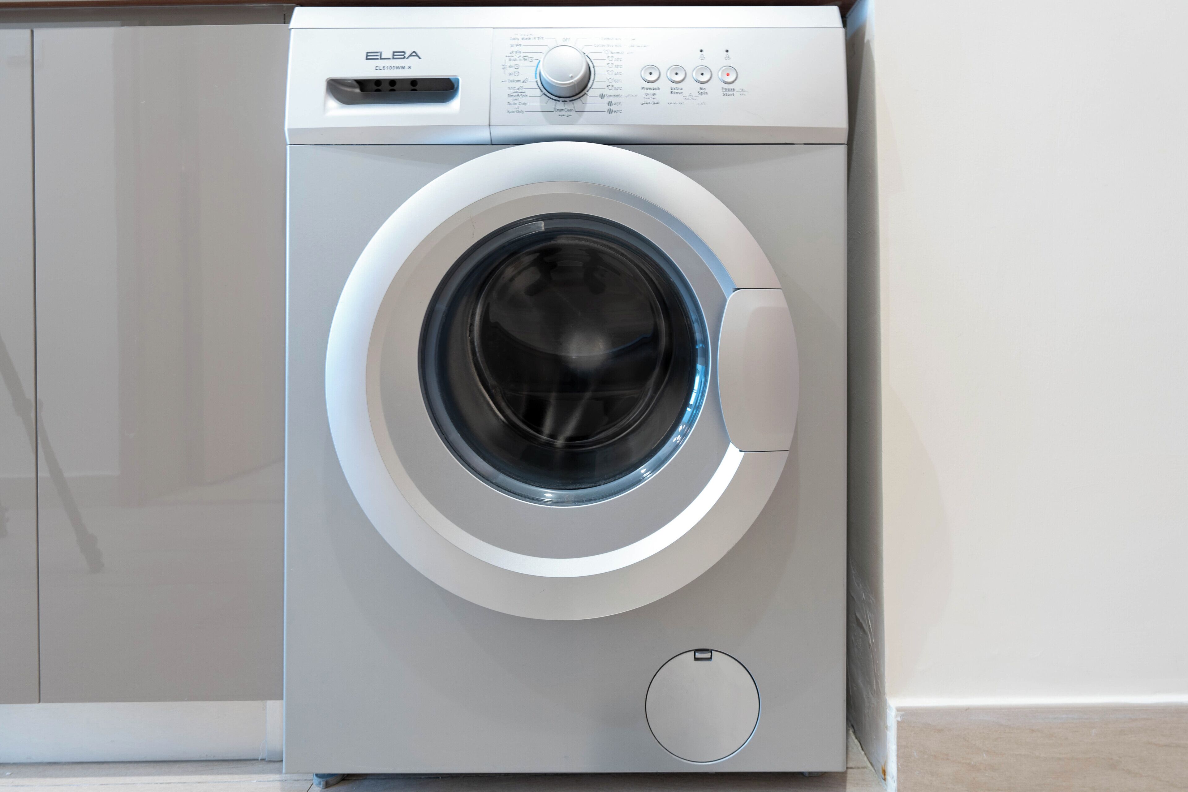 A front view of a modern, compact front-loading washing machine with a control panel and a small circular button below the door.