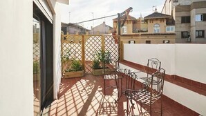 A balcony with a metal table and chairs, potted plants, and a view of neighboring buildings. - 1-BR flat with terrace -Eixample (Barcelona)