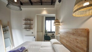 A bedroom with a wooden headboard, a bed with white linens, a woven light fixture, and a shelf with books. - 1-BR flat with terrace -Eixample (Barcelona)
