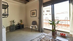 A living room with a sofa, a coffee table, a TV, and a window with curtains. - 1-BR flat with terrace -Eixample (Barcelona)
