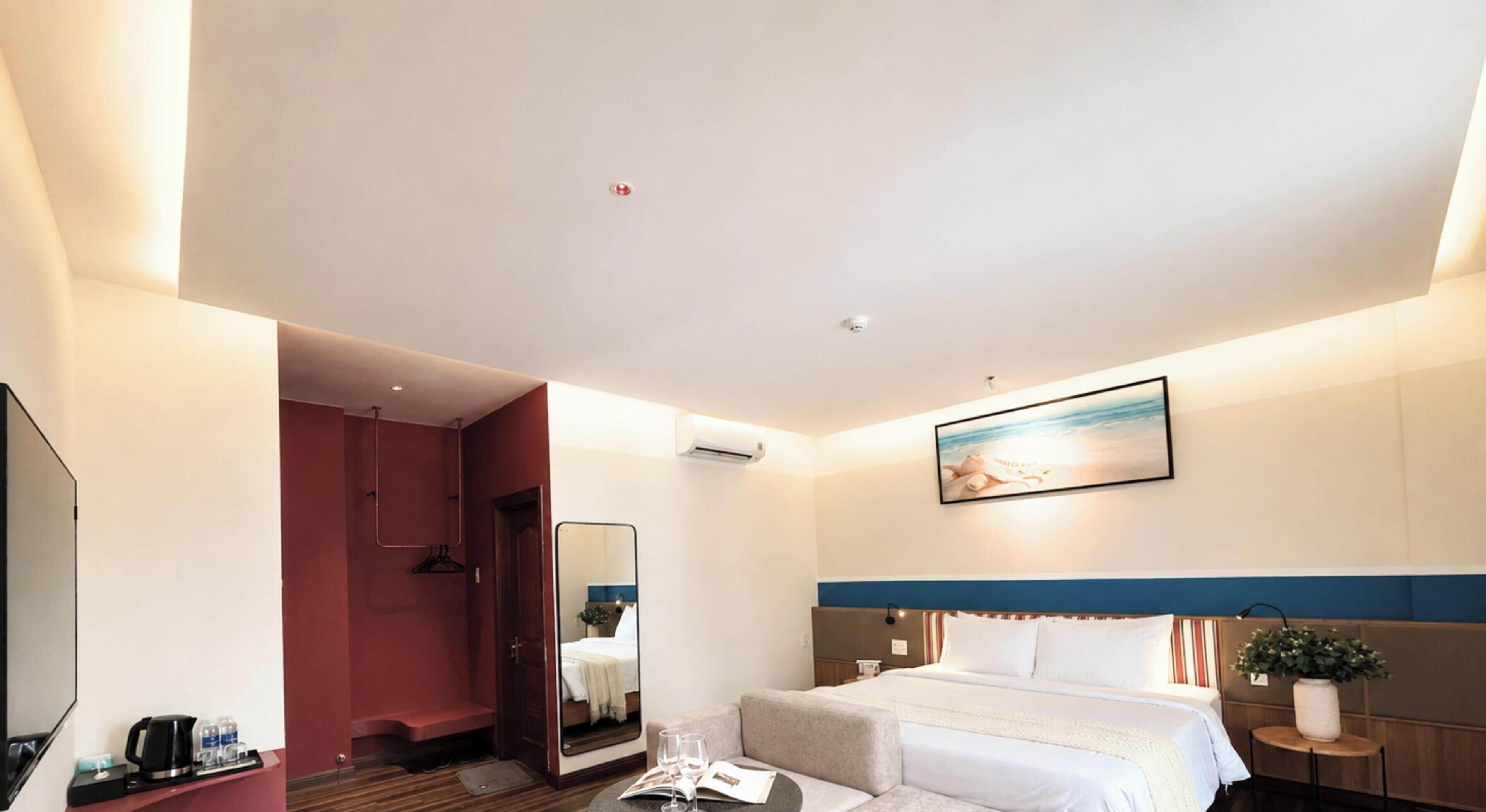 Ein Hotelzimmer mit Bett, Nachttisch, Spiegel, einem Gemälde und Blick auf den Strand.