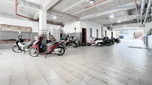 A spacious indoor parking area with multiple scooters parked, concrete ceiling with exposed beams, and tiled flooring. - Joi Boutique Bãi Sau  (Ho Chi Minh City)