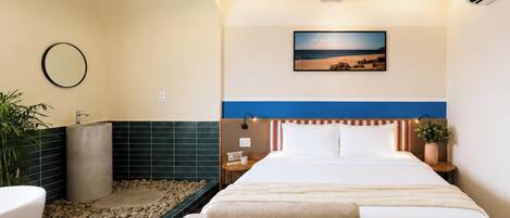 A hotel room with a bed, a bedside table, a nightstand, a mirror, a picture on the wall, and a small potted plant.