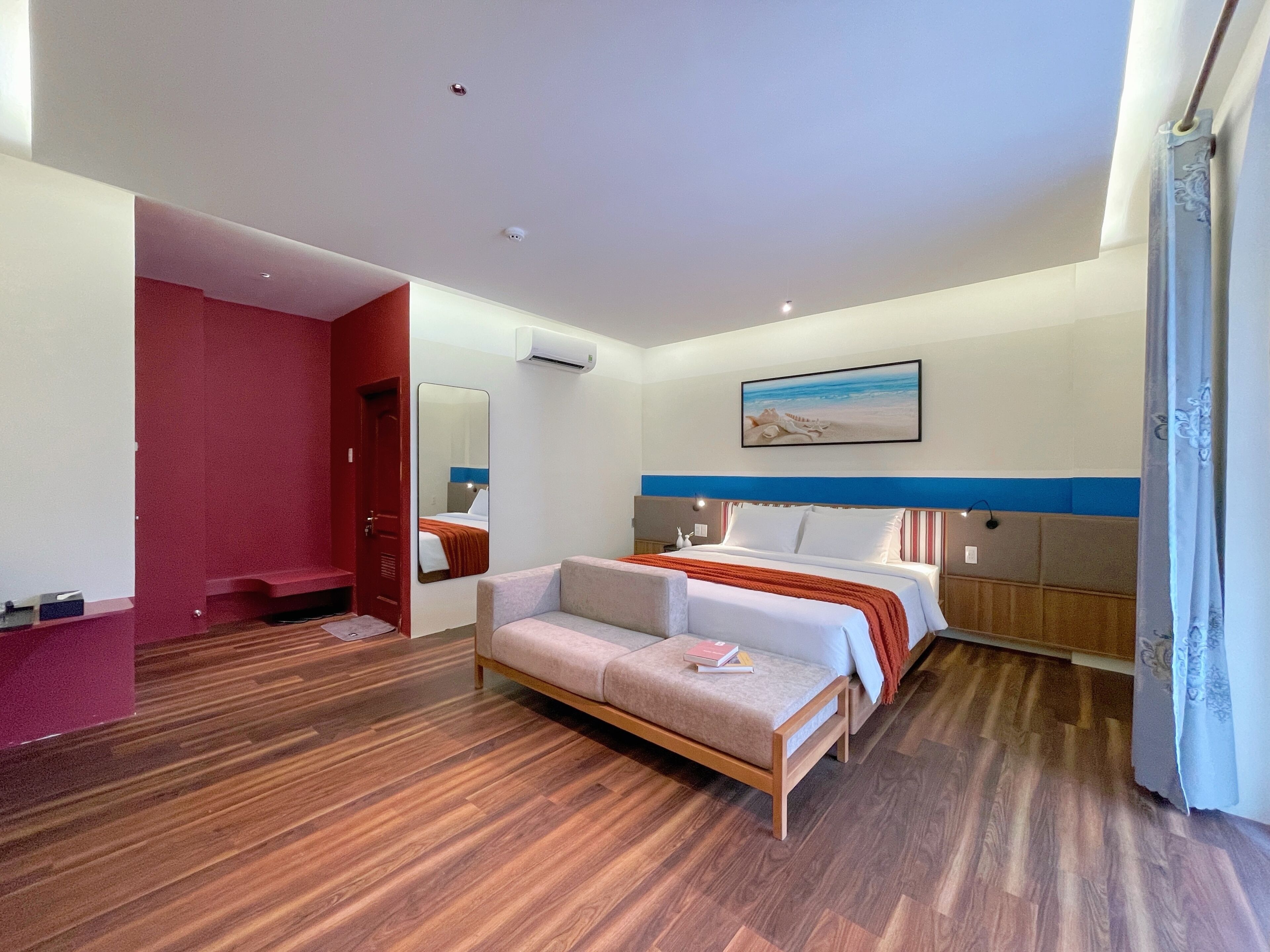 A hotel room with a bed, a sofa, a mirror, a painting, and a wooden floor.