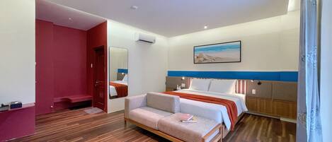 A hotel room with a bed, a sofa, a mirror, a painting, and a wooden floor.
