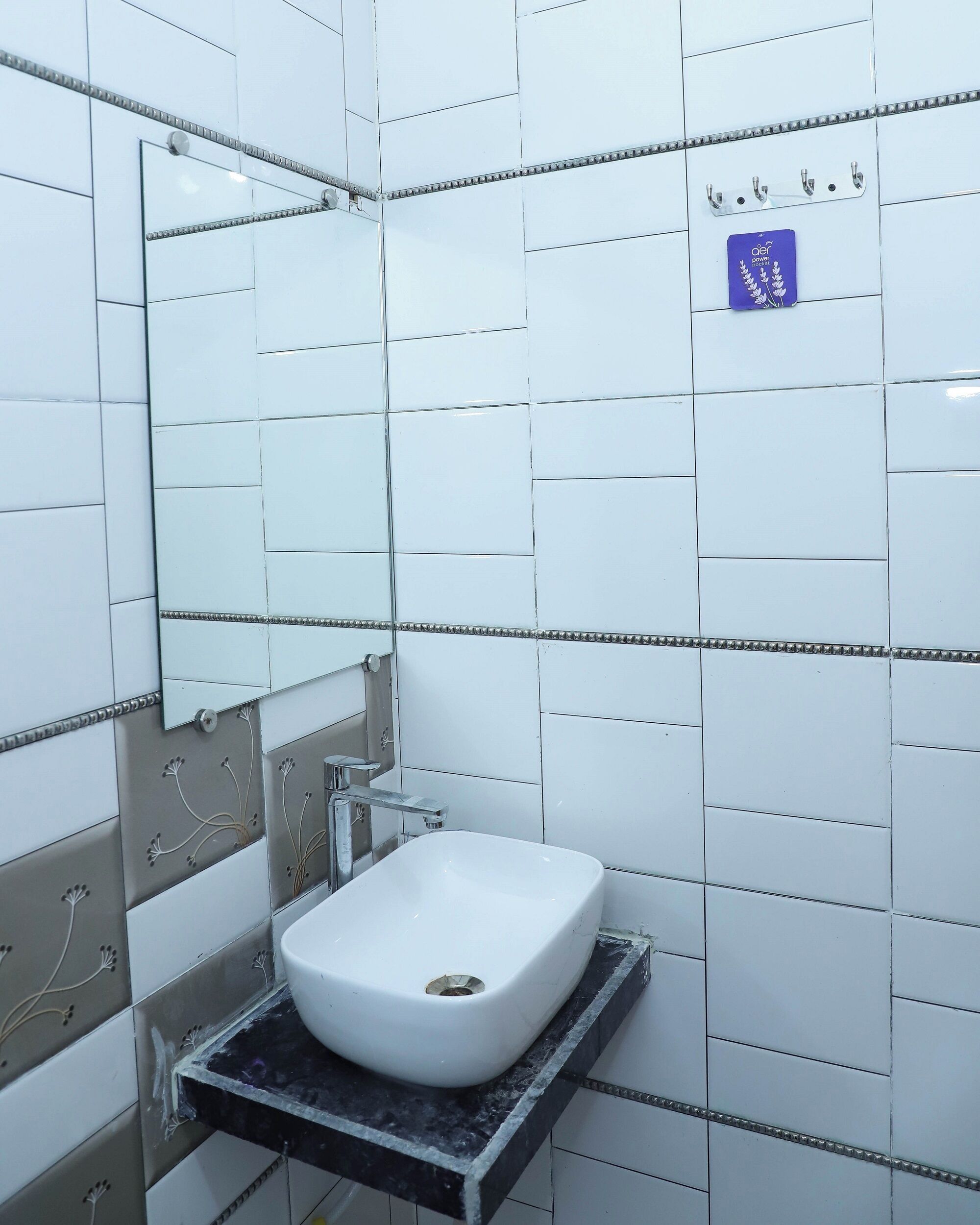 Un baño con paredes de azulejos blancos, un lavamanos rectangular con un solo grifo y un espejo sobre él.