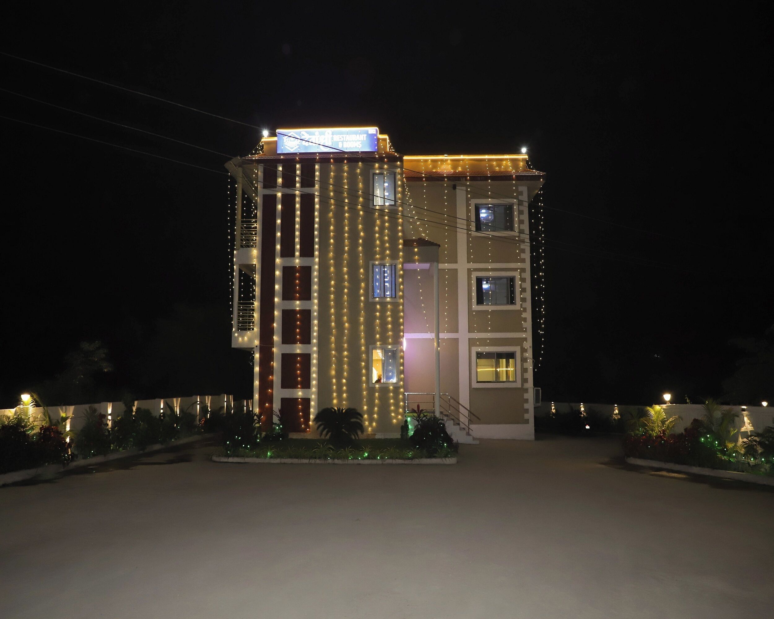 A multi-story building with vertical string lights, a sign indicating a restaurant, and a gated entrance.