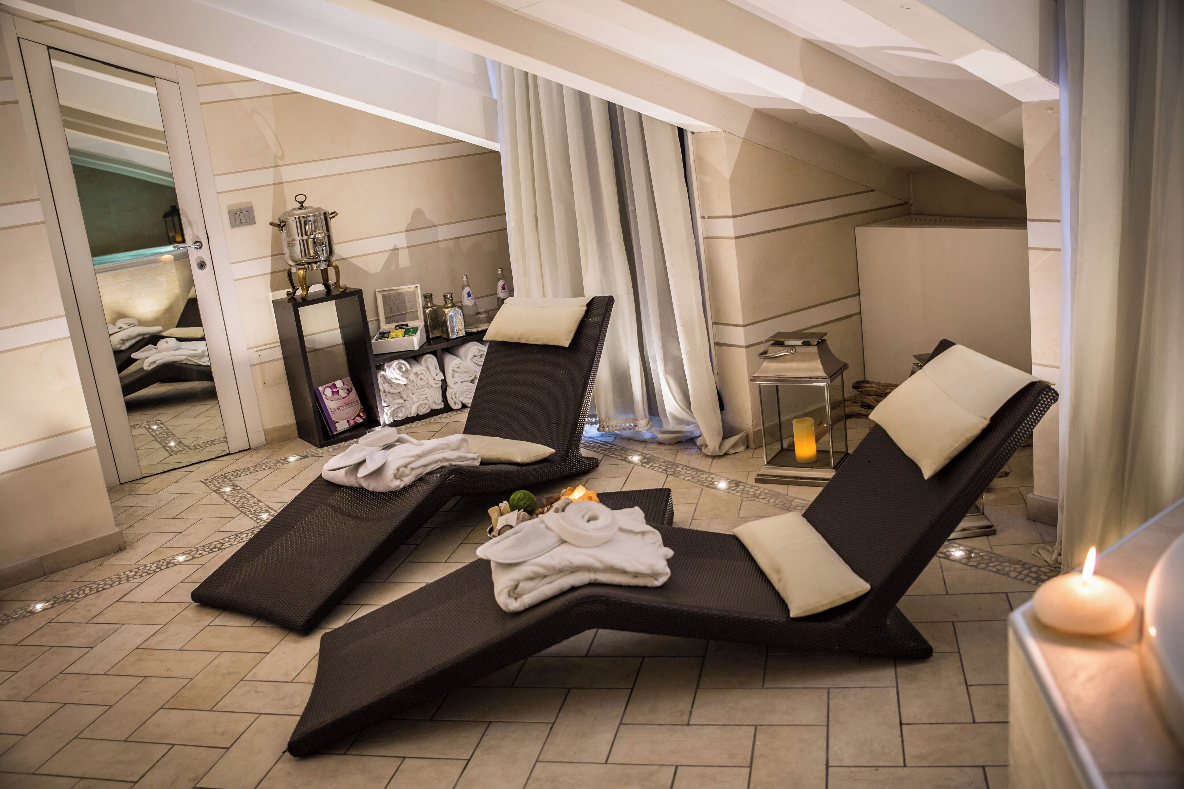 A spa room with two reclining chairs, a massage table, and a small table with candles and bottles.