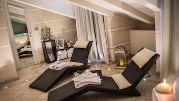 A spa room with two reclining chairs, a massage table, and a small table with candles and bottles.